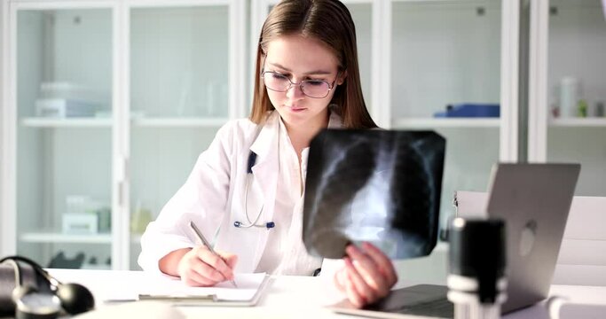 The young doctor holds an X -ray and writes a close-up. Diagnosis of the disease and injury, fluorography