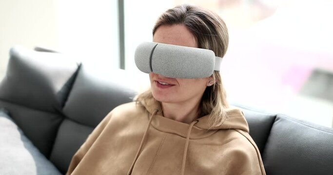 A young woman sits on a sofa with a virtual mask for sleeping, a close-up, an increased look. Relaxation device