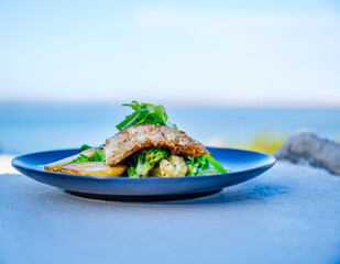 Samon fish with vegetables dish on a concrete table with blurred beach background at Paternoster, South Africa