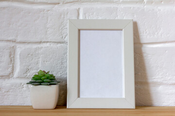 Mockup of a white photo frame and succulents in a vase on a table or shelf.