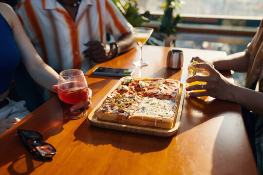 Closeup image of friends eating pizza and having drinks when hanging out in cafe