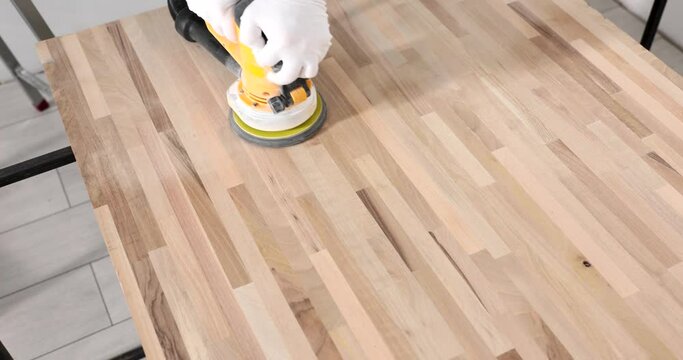 A man polishes a wooden laminate with a grinding machine, a close-up. The work of the carpenter