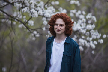 Man with curly red hair standing against a backdrop of spring blossoms