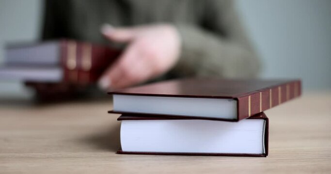 Female hands lays a stack of red books on the table, a close-up. Encyclopedic knowledge, education