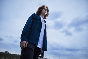 Red-haired man in contemplation under a moody sky, evoking introspection