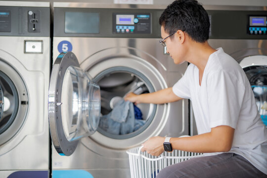 Young Asian Man putting up cloth into wahing machine, Man with luandry day.