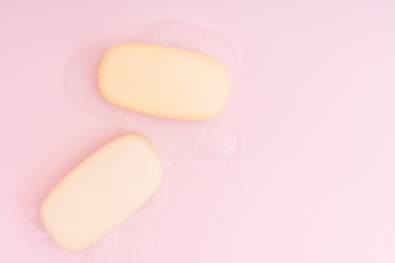 Two bars of soap with foam on a pink background.