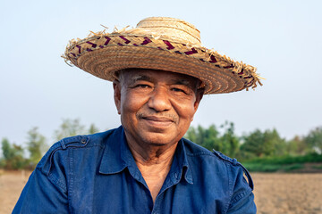 Portrait of elderly farmer man in straw hat standing on agricultural area and looking at the camera
