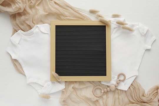 Pregnancy announcement template for social media, letterboard and two white bodysuits, waiting twins, aesthetic flat lay composition.