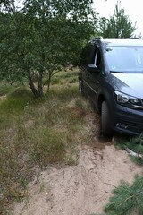 dark car stuck on dirt path surrounded by lush greenery, wheel partially buried in humid soil. concepts: adventure tourism, roadside assistance, vehicle difficulties, off-road driving skills