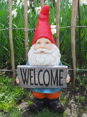 Funny Garden dwarf with a red pointed hat holding a welcome sign