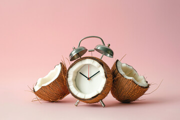 Alarm clock with half of a coconut instead clock face on pastel background. Creative minimalist concept, dieting tropical exotic healthy meal. Summertime, tropical vacation concept