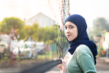 Muslim woman in hijab with brown eyes holding volleyball net in morning sunlight.