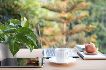 A cup of tea on a wooden work table outside with side view of Laptop and notebooks balcony outdoor