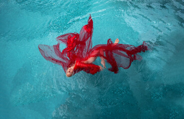 Top view to beautiful sexy blonde young sensual dreamy woman, swimming with red cloths wrapped in clear turquoise blue pool water