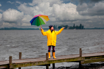 Junge Frau mit gelber Regenjacke und buntem Schirm auf einem Steg
