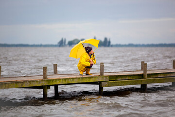 Junge Frau mit gelber Regenjacke und Schirm in der Hocke auf einem Steg