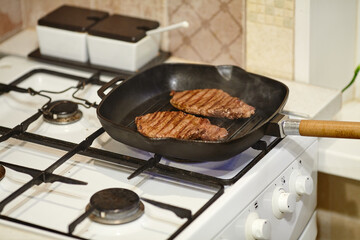 The process of cooking two beef steaks in frying pan, the hands of male chef salting raw meat, close-up