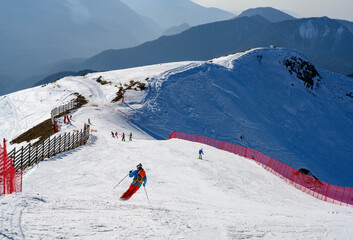 Downhill skiing with skiers in the Caucasus Mountains with silhouettes of mountain peaks far to the...
