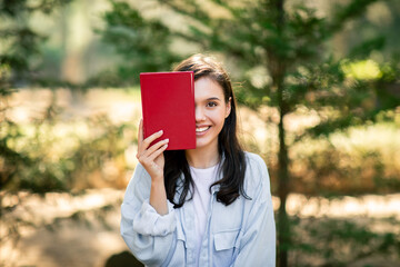 Woman holding red book covering half her face - 779029616