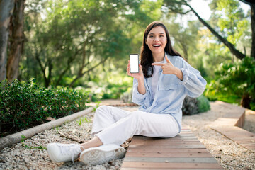 Happy woman showing phone screen outdoors at public park