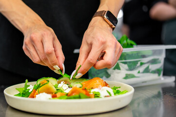 A chef meticulously garnishes a vibrant, fresh salad with green herbs, showcasing culinary artistry...