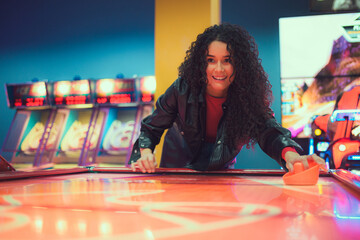 Excited young woman enjoying an air hockey game at a vibrant arcade