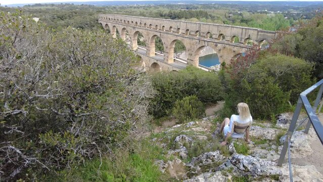 Female traveler gazes out at the UNESCO world heritage site, Pont du Gard, in the serene landscape of Provence in France.