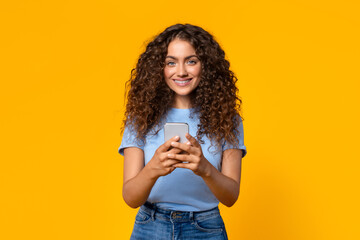Content woman using a smartphone on yellow