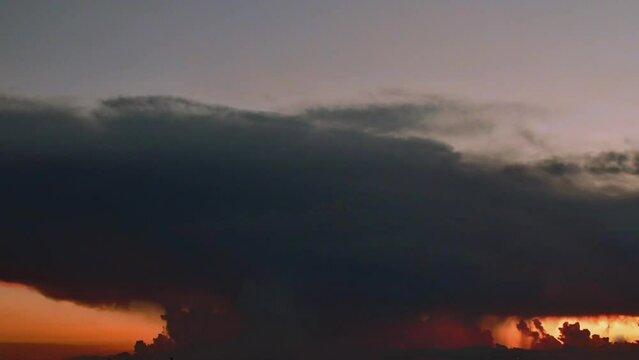 Timelapse shot.    A very large storm cloud looms in the sky showcasing dramatic rolling storm clouds and flashes of lightning Dramatic rolling storm clouds with flashes of lightning