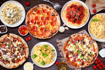 Delicious Italian food table scene. Assortment of pizzas and pastas. Top view on a dark wood background.