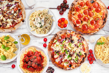 Delicious Italian food table scene. Assortment of pizzas and pastas. Above view on a white wood background.