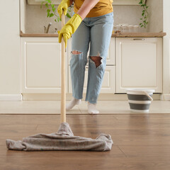 A woman mops the floor in her home kitchen. Female hands in yellow gloves while cleaning the kitchen