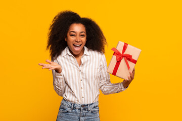 Excited woman holding a gift box on yellow background