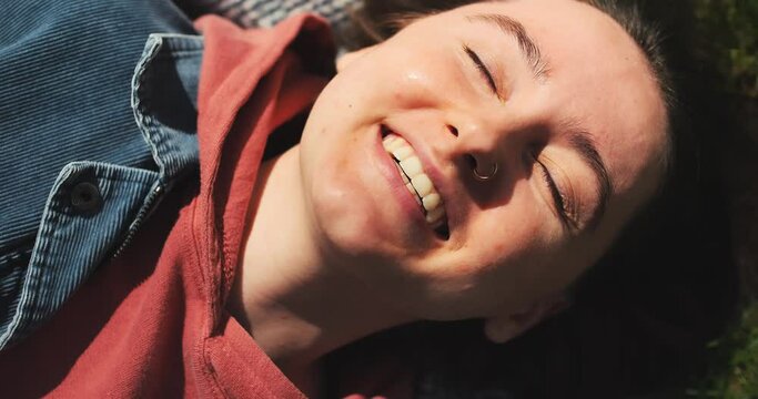 Closeup happy girl lying on green grass. Beautiful woman enjoying sunny spring in park. Relaxed young adult female in nature. Portrait of happy woman