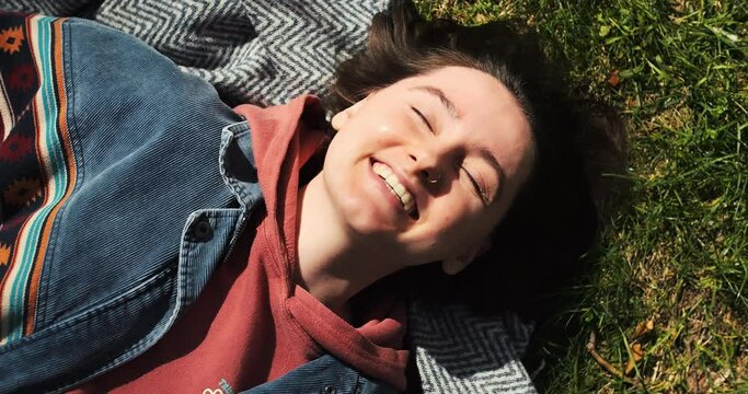 Closeup happy girl lying on green grass. Beautiful woman enjoying sunny spring in park. Relaxed young adult female in nature. Portrait of happy woman