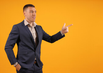 Man in a suit pointing to the right, looking in the same direction, against an orange background, appears instructive.