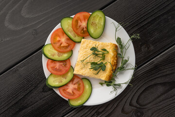 Close-up of a slice of quiche with fresh vegetables and pea shoots on a plate