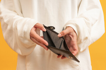 Hands holding an empty black wallet with yellow background