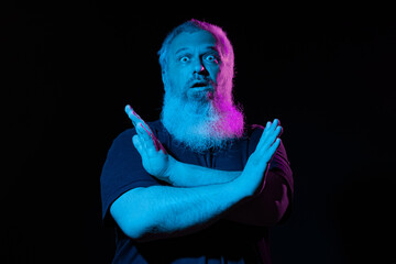 Man with a glowing pink beard under blue lighting, crossing his arms in an 'X' shape, against a dark background.