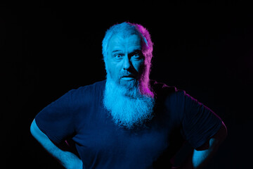 A bearded man stands with a stern expression, under blue and pink neon light casting shadows.