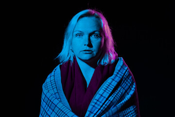 A woman with a stern expression, lit by blue and purple neon lights, wearing a scarf
