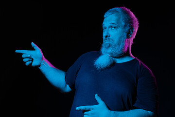 A bearded man pointing sideways with one hand and other on his belly, pink and blue lights casting a vibrant glow.