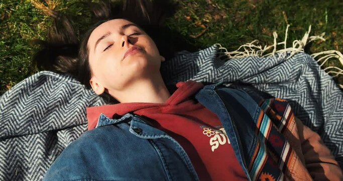 Closeup happy girl lying on green grass. Beautiful woman enjoying sunny spring in park. Relaxed young adult female in nature. Portrait of happy woman