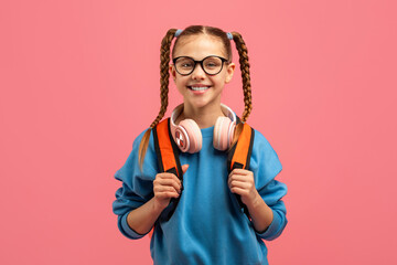 Smiling girl with headphones and backpack on pink background
