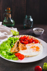 Appetizing tacos with fried egg, bacon, tomato and lettuce on a plate on the table vertical view