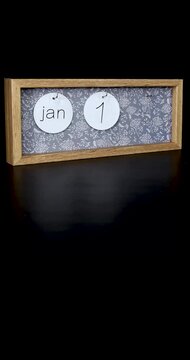 Portrait footage of a wooden calendar block showing the date January 19th with a mans hand putting on and taking off the metal discs with the date and month on them