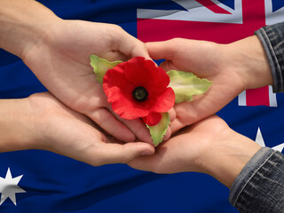 Anzac is the Australian national holiday. Hands with poppy buds on national flag background.