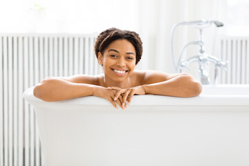 Smiling African American woman peeking from bathtub