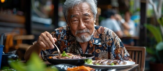 An old Asian man is sitting at a table, eating food from a bowl placed in front of him.